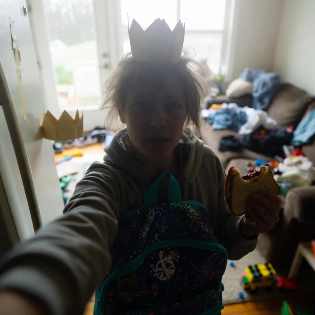 Frazzled parent juggling backpack and sandwich in chaos.