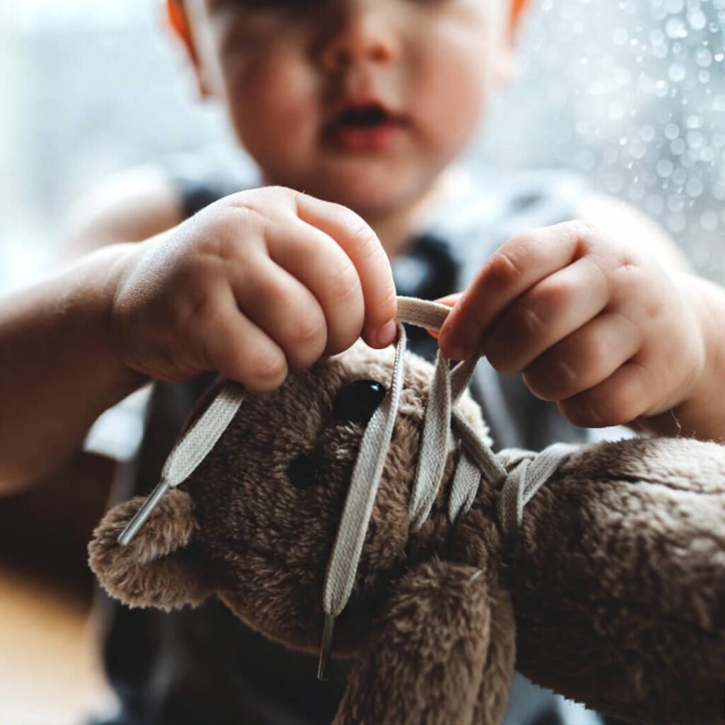 Child tying shoelaces on teddy bear, rainy day