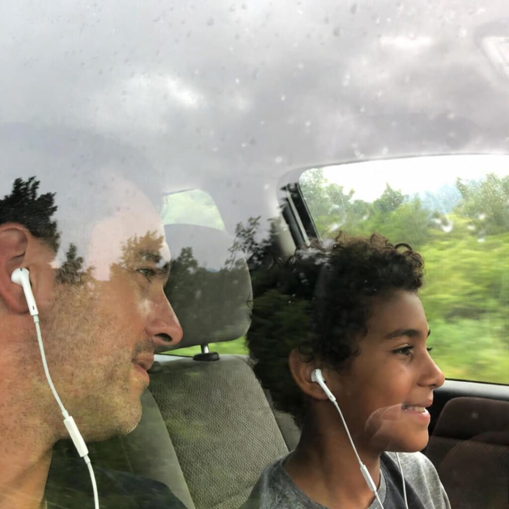 Parent and kid sharing earbuds through rainy window